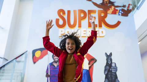 Young child jumping joyfully in front of a superhero sign