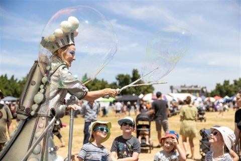Performer with a bubble wand surrounded by children
