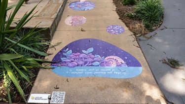 Vinyl artwork with purple floral patterns applied to a path beside plants and garden edging.