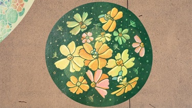 Close‑up of a green circular vinyl artwork with yellow floral patterns applied to pavement.