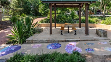 Wide view of landscaped seating area with multiple circular vinyl artworks installed along the surrounding path.