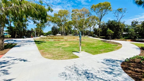 Image shows paved concrete in the forground, with trees and ampithere seating in the distance