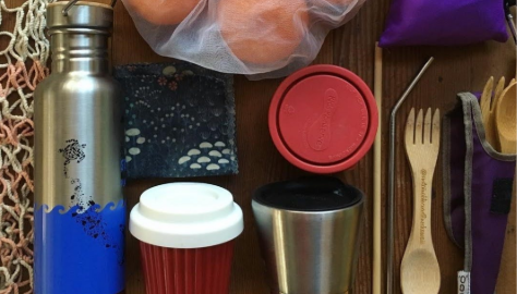Reusable household items including a metal water bottle, reusable coffee cups, feed containers, cutlery, a metal straw, and reusable bags.