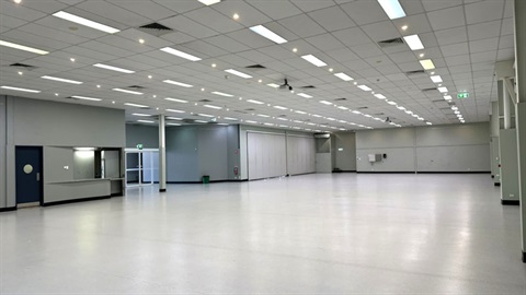 Large empty indoor hall with bright lighting, white floor and rows of ceiling panels.