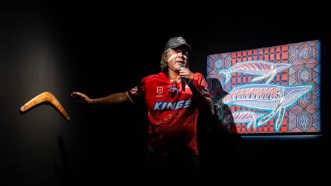 First Nations man with boomerang and digital screen in background