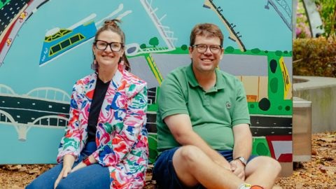 Man and woman sitting on sand with artwork backdrop