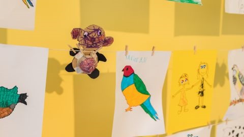 Children's artworks pegged on a string in front of a yellow wall
