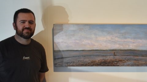 Artist Aaron Butt standing in front of landscape painting