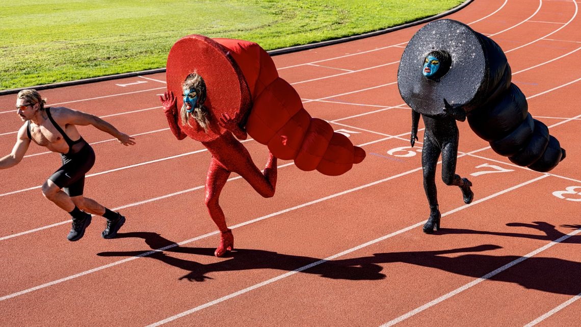 A male runner and two people in costume on an athletics track