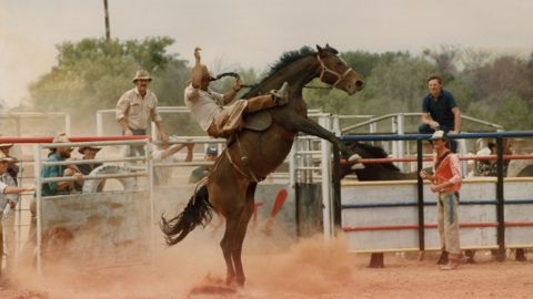 Man riding a bucking bronc at a dusty rodeo