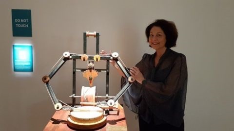 Woman standing next to wooden model of a Da Vinci invention