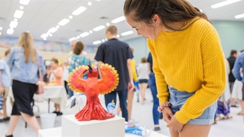 A girl in a yellow jumper looking at a bird sculpture.