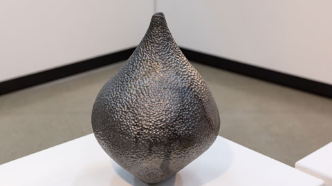 A clay distilled form in metallic finish on a white pedestal 