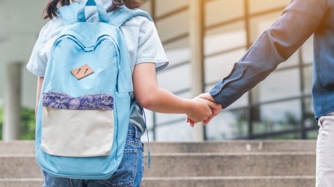 Rear view of a young girl with backpack holding a man's hand
