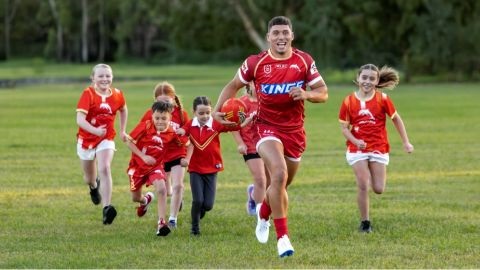Dolphins NRL player in red jersey being chased by kids