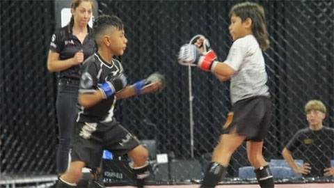 Two young MMA fighters standing across from each other with fists risen, there's a referee in the background and a supporter outside of the cage.