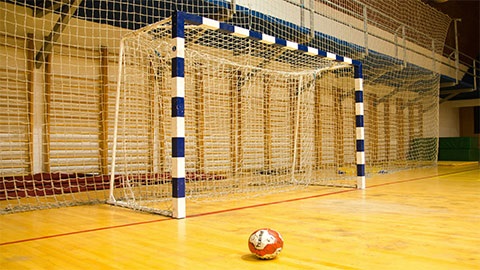 An indoor soccer goal post with a soccer ball on the wooden floorboards.