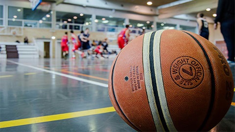 A basketball in the foreground, in the background is are two teams of basketballers playing for the win.