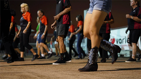 An image of people wearing cowboy boots, standing in line in the middle of a line dance.