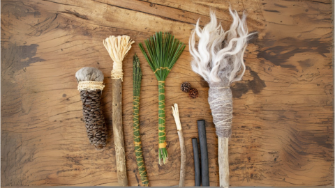 Camera is angled down facing a wooden table. On the table is various handmade art brushes from fibres, grasses and seeds.