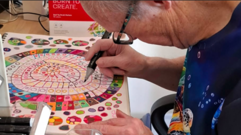 a man with glasses and wearing blue, holding a marker and creating art