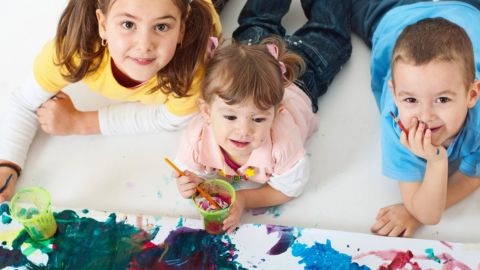 3 children lying on the floor painting