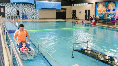 Man pushing kid in a wheelchair down a ramp into a pool.