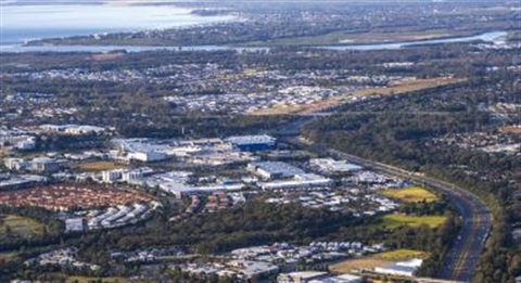An aerial view of City of Moreton Bay. The ocean is in the far left corner stretching into an inland river. The image has trees, roads and some big buildings.