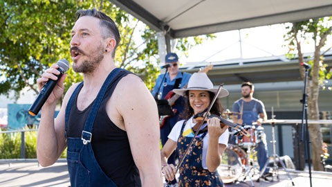 A band playing outside with a singer, violinist, base guitarist and drummer