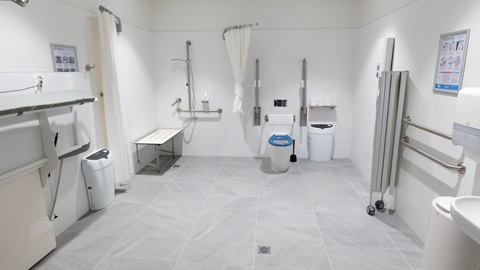 Accessible bathroom with grab rails, shower chair, toilet and wide open space for mobility access.