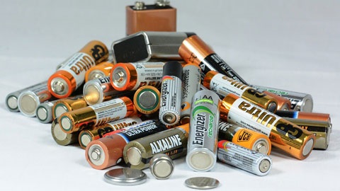 Pile of various household batteries including AAA, AA, C, D and 9V batteries