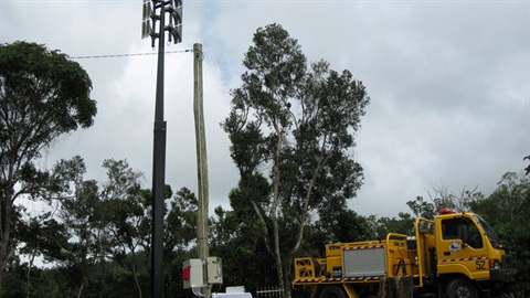 An emergency early warning system mounted on a tall pole among trees, with maintenance equipment positioned nearby.
