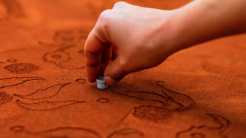 Orange fabric with leaves cut in it and a hand ushing a thing in to make a circle.