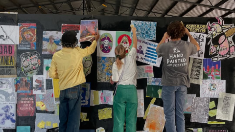 Three people with their backs facing the camera putting up artworks on a black board