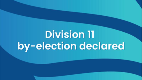 Graphic with blue wave patterns and the text “Division 11 by‑election declared.”