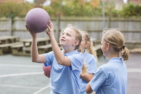 Children in light blue uniforms playing with a ball on an outdoor court.