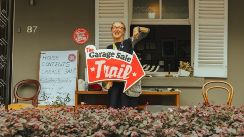 Woman smiling holding a sign that says Garage Sale Trail.png