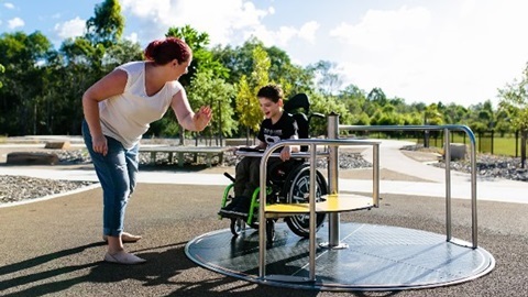 Women pushing a child living with disability on inclusive playground equipment