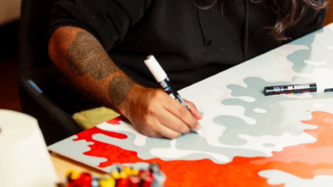 A person with a tattoo on their arm creating art with red and blue pens
