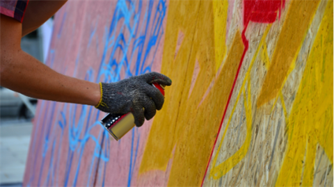 a person out of the screen holding a red spray paint can and using it on a canvas. The person out of frame has used yellow, red, pink, and blue to create an image