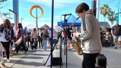 Young man on stage playing saxophone with people watching in the background 