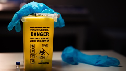 Yellow sharps container with needle and blue gloves on top