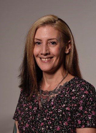 Daniella D'Cruz, a blonde haired women smiling at the camera in a black floral short.