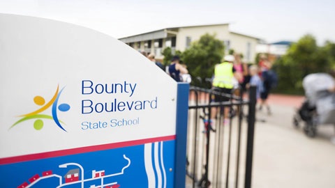 School welcome sign for Bounty Boulevard State School, with the gate and people in the background.