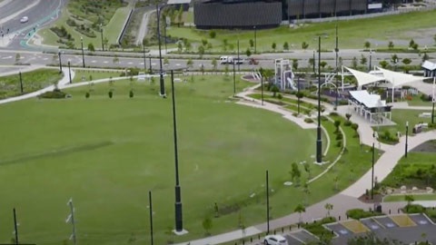 Ariel view of a large green park with paths, light poles and small buildings.